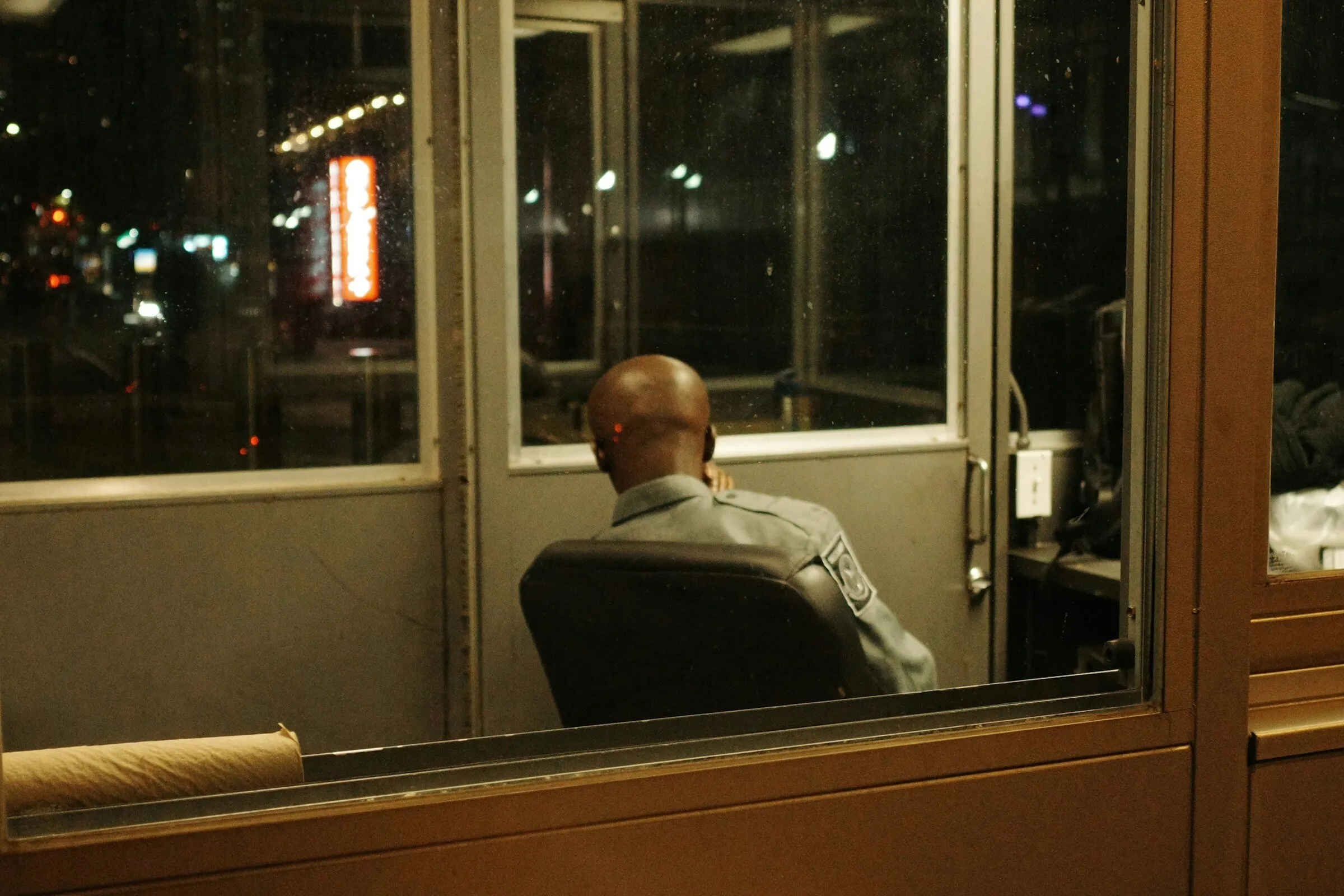 A security guard on post in a lit booth at night